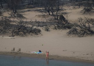 Ani požáry a spáleniště neodradily turisty od hrátek u moře, jako ve čtvrtek 27. července 2023 na pláži poblíž vesnice Gennadi na ostrově Rhodos v jihovýchodním Řecku v Egejském moři.