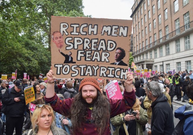 Demonstrant drží transparent zobrazující Farage, Muska a Zuckerberga během pochodu proti rasismu a fašismu a na podporu migrantů na Russell Square. Zatímco krajně pravicoví demonstranti v čele s Tommym Robinsonem pořádají vlastní shromáždění před Downing Street pod názvem „Unite The Kingdom“.