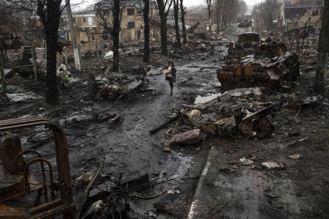 žena prochází mezi troskami ruských tanků zbytky ulice v Buči