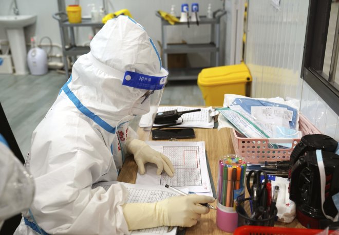 Zaměstnanec nemocnice v čínské Šanghaji je kvůli koronavirovým opatřením oblečen v ochranném obleku.