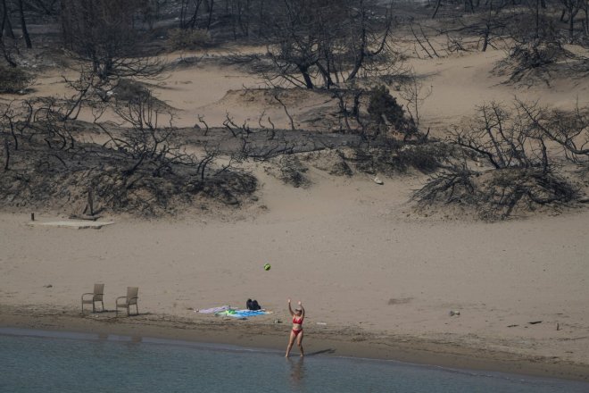 Ani požáry a spáleniště neodradily turisty od hrátek u moře, jako ve čtvrtek 27. července 2023 na pláži poblíž vesnice Gennadi na ostrově Rhodos v jihovýchodním Řecku v Egejském moři.