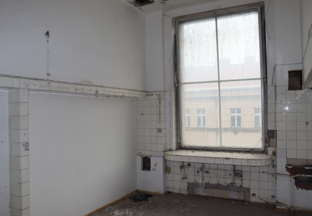Pohled do malé místnosti ve 4. patře, kde se směrem do ulice nacházely 2 operační sály. Vyobrazená místnost se nacházela mezi nimi a původně sloužila sestrám, které odtud měly obsluhovat dle potřeby oba operační sály.