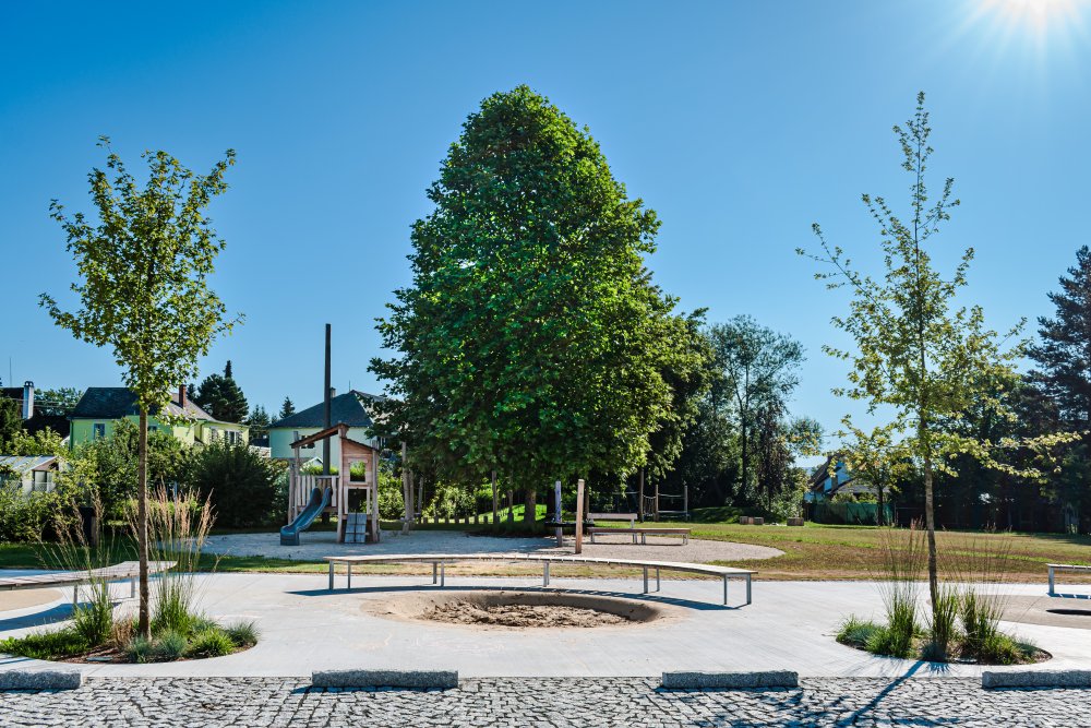 Příšovice nemají jasný střed. V obci je několik míst, která mají potenciál tuto funkci plnit. Řešené místo u Sokolovny je jedním z nich. Ambicí projektu bylo původně mrtvý plácek mezi Sokolovnou a potokem Příšovkou nejen zrekultivovat, ale vytvořit z něj živý veřejný prostor. (atakarchitekti)