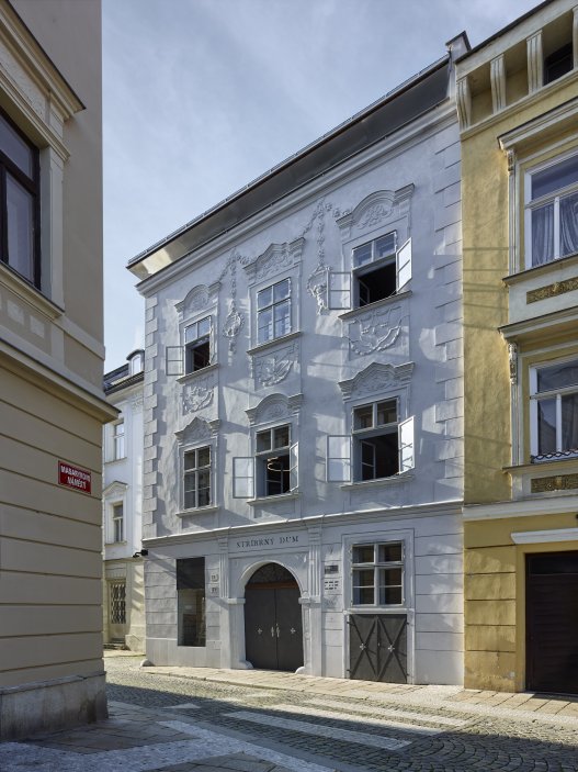 Dům se nachází na spodní straně hlavního Masarykova náměstí v Jihlavě. Jedná se o urbanisticky i architektonicky hodnotný objekt pod památkovou ochranou. Je typickým příkladem měšťanského domu na jihlavském náměstí, které představují nejhonosnější stavby svého druhu u nás. Obnova nevyužívaného domu byla spojena s nalezením vhodného využití, založeném na zájmu o životaschopnost a zpřístupnění velmi cenné architektonické památky veřejnosti.