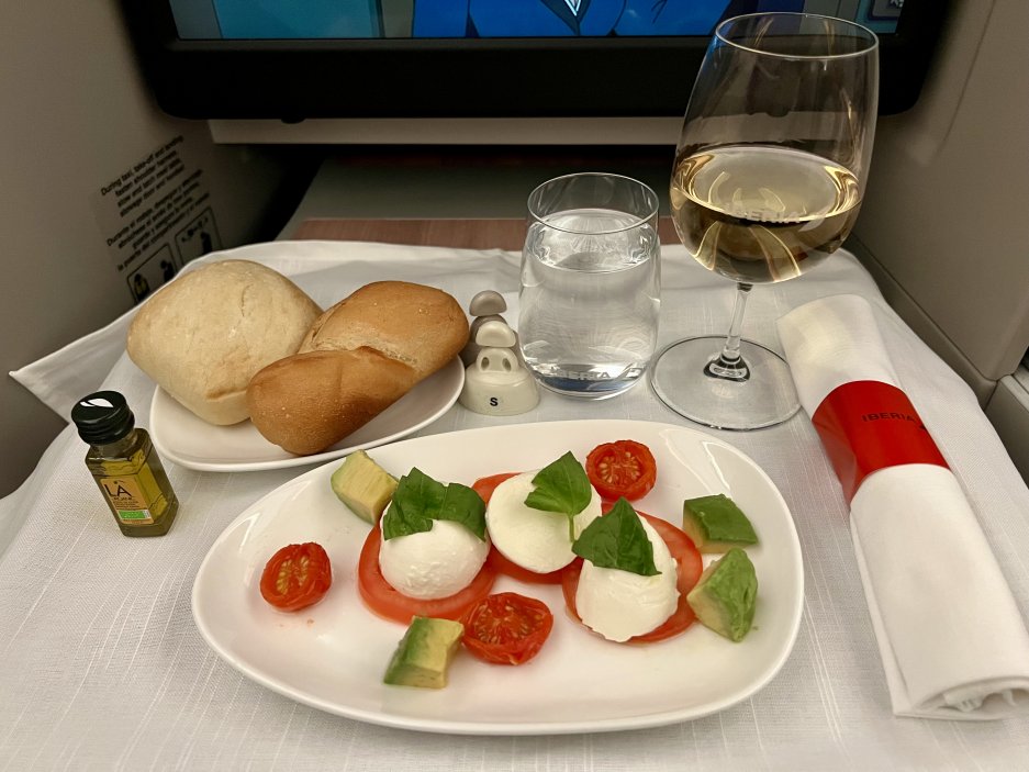 Předkrm caprese – mozzarella, rajčata, avokádo, pečivo a sklenka bílého vína