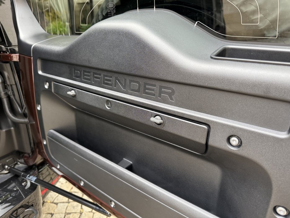 Detail výplně zadních dveří s výrazným nápisem Defender, připomínající odolnost a funkčnost.