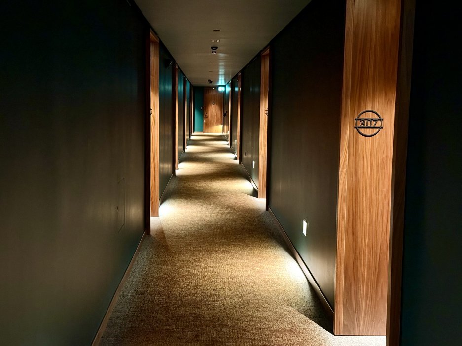 Chodba hotelu v kombinaci tmavých stěn a dřeva působí útulně a elegantně