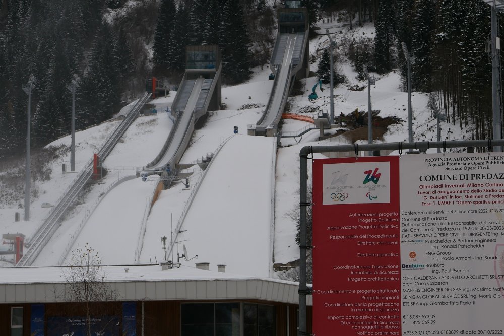 Rekonstrukce skokanského areálu v Predazzu pro Zimní olympijské hry Milano-Cortina 2026 představuje citlivý kompromis mezi sportovním prestiží, tlakem na udržitelnost a obrovskými veřejnými investicemi. Z ekonomického pohledu se projekt pohybuje v desítkách milionů eur