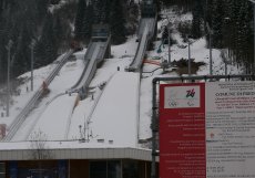 Rekonstrukce skokanského areálu v Predazzu pro Zimní olympijské hry Milano-Cortina 2026 představuje citlivý kompromis mezi sportovním prestiží, tlakem na udržitelnost a obrovskými veřejnými investicemi. Z ekonomického pohledu se projekt pohybuje v desítkách milionů eur