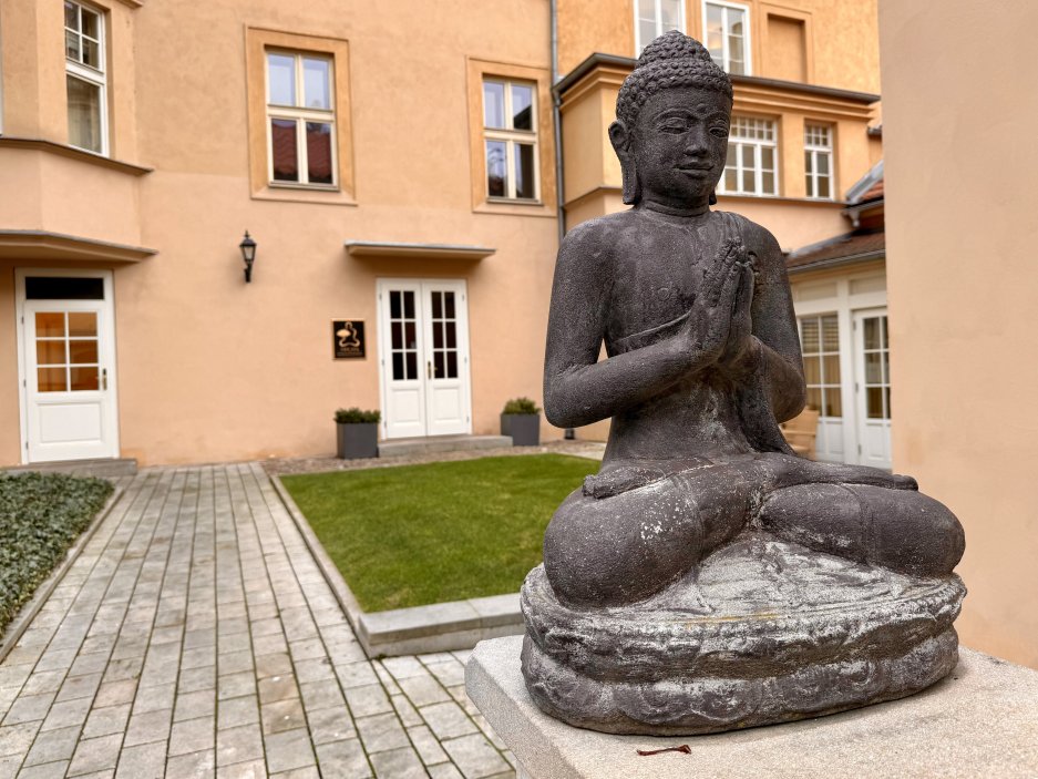 Vnitřní klášterní dvůr hotelu s buddhistickou sochou. Historické prostředí výrazně přispívá k atmosféře klidu a odstupu od města