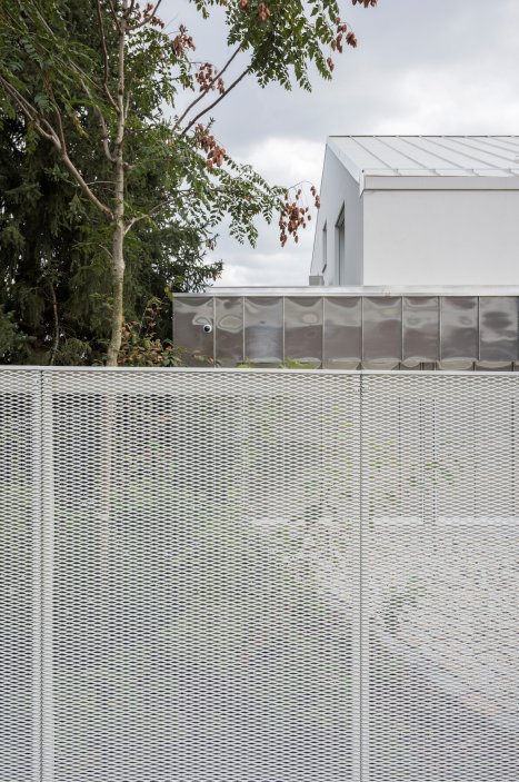 Výsledný dvojdům charakterizují terasy orientované na jih umožňující po svém obvodu výsadbu vyšší zeleně. Hmota je řešena jako ustupující bílý blok kopírující terén. Na bočních fasádách jsou dle výhledů z interiéru komponovány různé typy čtvercových oken. Na úrovni ulice je tento bílý monolit protnut horizontálním objemem garáží opláštěným přírodním hliníkovým falcovaným plechem.