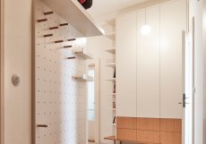 Perforovaná systémová stěna na police a háčky vytváří funkční i vizuální motiv, který se opakuje napříč bytem.