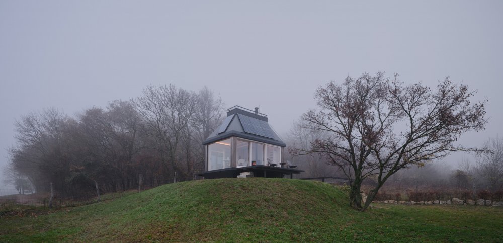 Minimalistický víkendový dům stojí na okraji vinic nad hradem Devín a nabízí jedinečné výhledy do krajiny. Díky odklápěcím fasádám se interiér otevírá do dvou teras a propojuje se s okolní přírodou. Kompaktní prostor ukrývá vše potřebné včetně kuchyně, koupelny i skrytého spaní v podkroví. Dominantním prvkem je velkoformátové zasklení, které přivádí do interiéru maximum světla.
