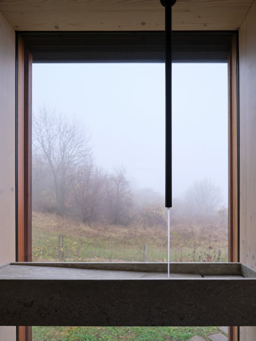 Minimalistický víkendový dům stojí na okraji vinic nad hradem Devín a nabízí jedinečné výhledy do krajiny. Díky odklápěcím fasádám se interiér otevírá do dvou teras a propojuje se s okolní přírodou. Kompaktní prostor ukrývá vše potřebné včetně kuchyně, koupelny i skrytého spaní v podkroví. Dominantním prvkem je velkoformátové zasklení, které přivádí do interiéru maximum světla.