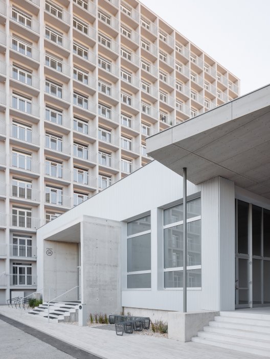 Monochromatická šedá barevnost zvýrazňuje pravidelnou geometrii původní prefabrikované konstrukce.