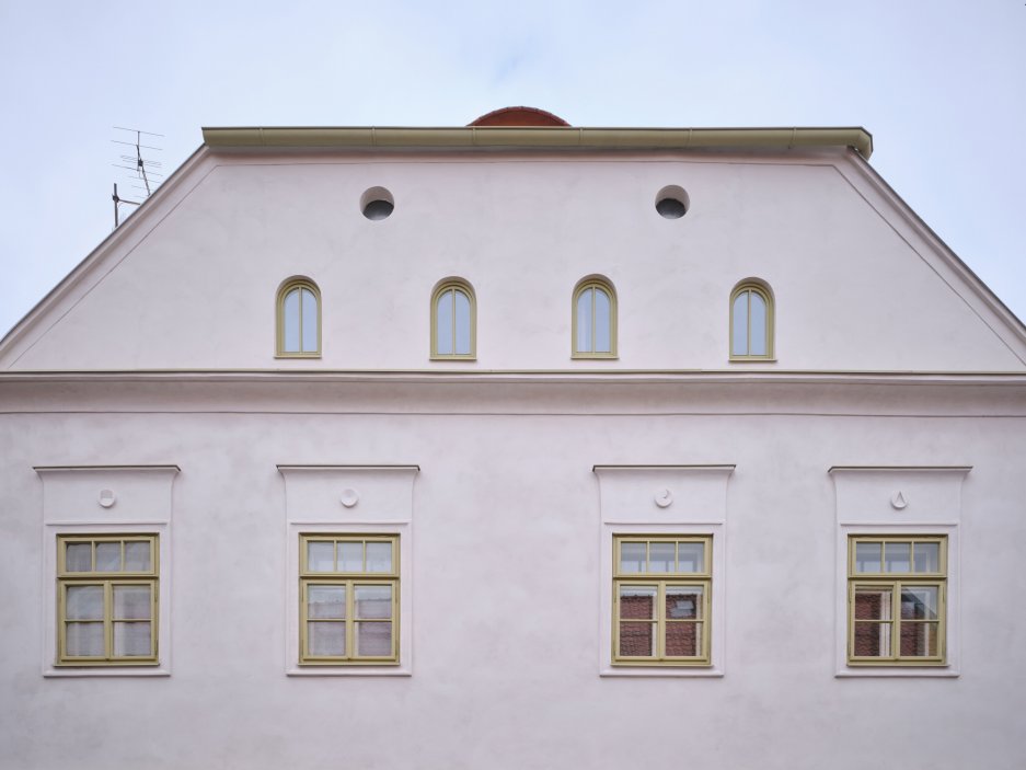 Architekti Jan a Barbora Horovi ze studia ORA proměnili rodinný dům v žatecké Obloukové ulici z téměř ztracené ruiny v místo, kde se potkává ubytování, výčep a soukromé zázemí. Rekonstrukce trvala osm let a stála na snaze zachovat maximum původních konstrukcí, využít recyklované materiály a nechat starý dům stárnout dál — jen s novým životem.