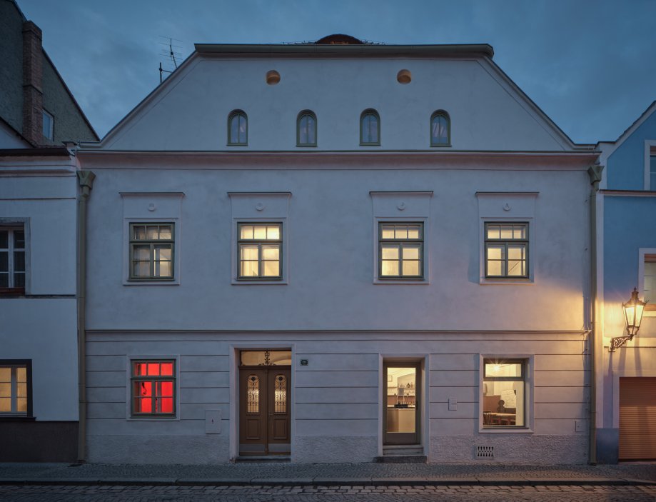Architekti Jan a Barbora Horovi ze studia ORA proměnili rodinný dům v žatecké Obloukové ulici z téměř ztracené ruiny v místo, kde se potkává ubytování, výčep a soukromé zázemí. Rekonstrukce trvala osm let a stála na snaze zachovat maximum původních konstrukcí, využít recyklované materiály a nechat starý dům stárnout dál — jen s novým životem.