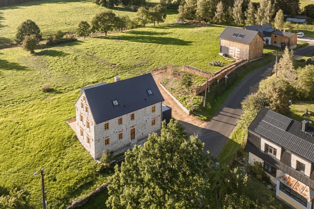 V Lipné u Hazlova, v krajině bývalých Sudet nedaleko německých hranic, stojí vedle sebe roubený statek po babičce majitele a kamenný dům z roku 1852. Obě stavby prošly citlivou obnovou, která zachovala původní dřevo a kámen a doplnila je současnou architekturou. Dnes tvoří komorní areál, kde hlavní roli hrají historie, krajina a klid.