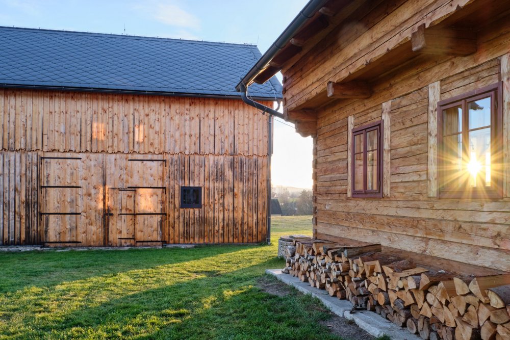 V Lipné u Hazlova, v krajině bývalých Sudet nedaleko německých hranic, stojí vedle sebe roubený statek po babičce majitele a kamenný dům z roku 1852. Obě stavby prošly citlivou obnovou, která zachovala původní dřevo a kámen a doplnila je současnou architekturou. Dnes tvoří komorní areál, kde hlavní roli hrají historie, krajina a klid.
