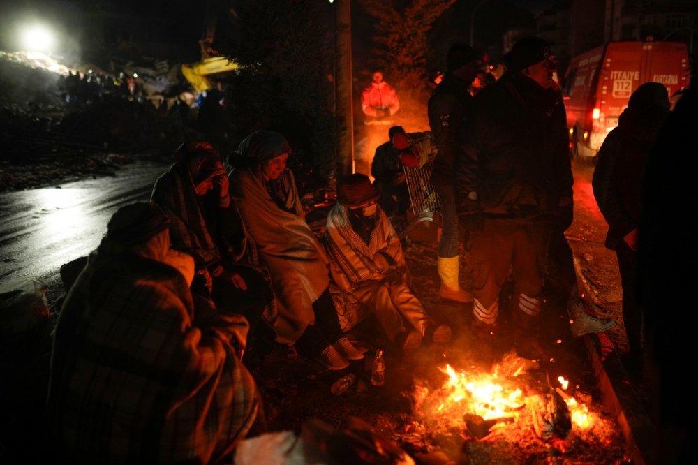 Lidé se zahřívají u ohně, zatímco záchranné týmy hledají po zemětřesení lidi v Elbistánu v jižním Turecku, středa 8. února 2023.