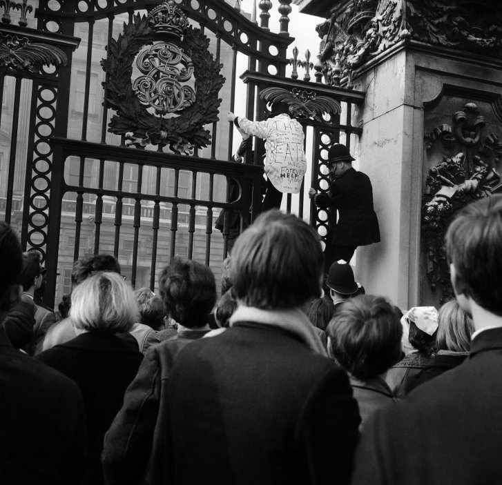 Beatlemánie před Buckinghamským palácem. V době, kdy členové Beatles přebírali Řád britského impéria, někteří fanoušci se snažili přelézt brány paláce.
