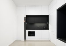 Světlé, hladké plochy maximalizují volný prostor. Prázdné objemy pohovky a kuchyně jsou s nimi záměrně v kontrastu. Prázdná stěna slouží jako promítací plátno.
